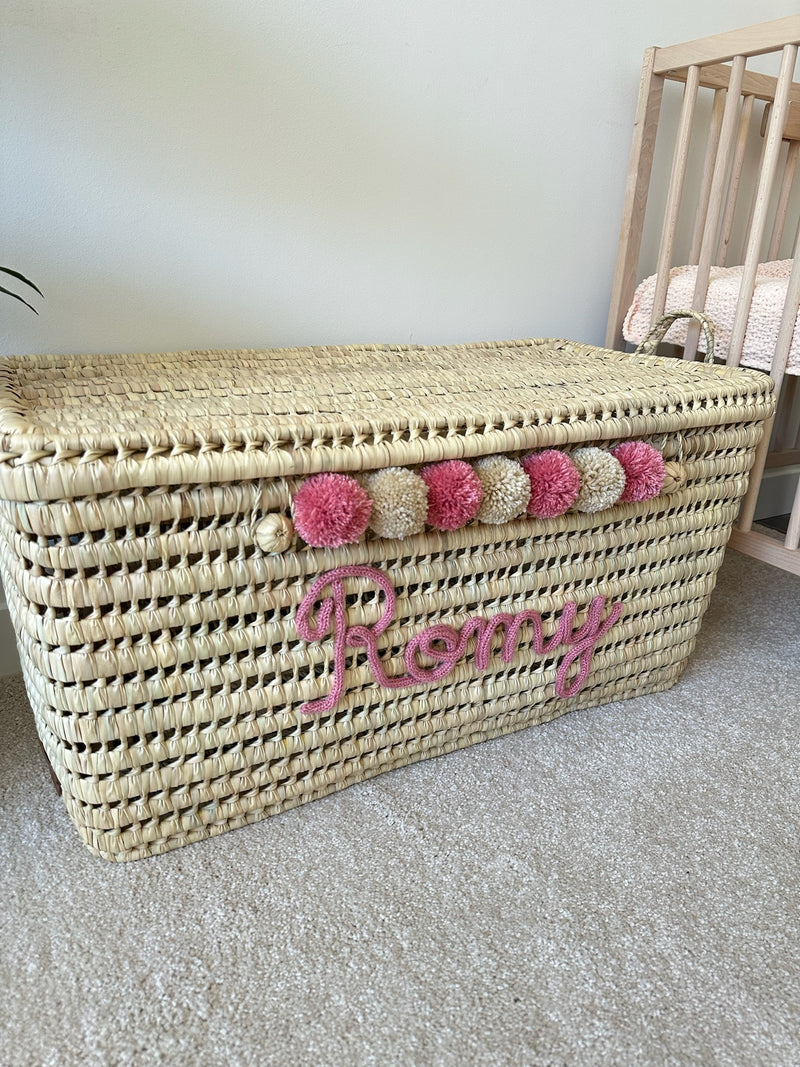 Malle de rangement en osier personnalisée avec prénom Remy en tricotin rose et pompons roses et beiges, vue de côté
