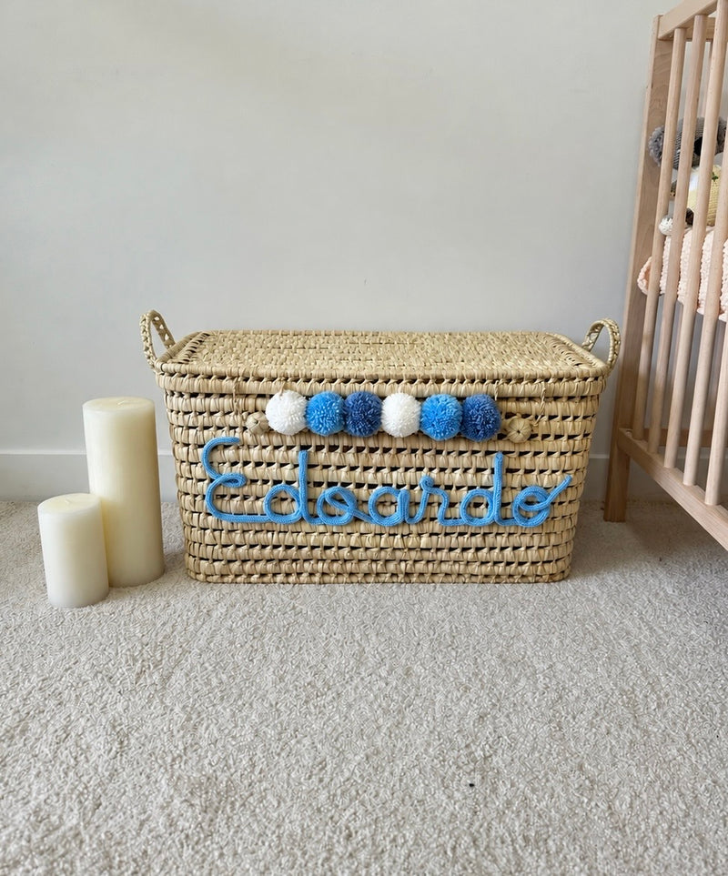 Coffre à jouets en osier personnalisé avec prénom en tricotin bleu et pompons bleus et blancs